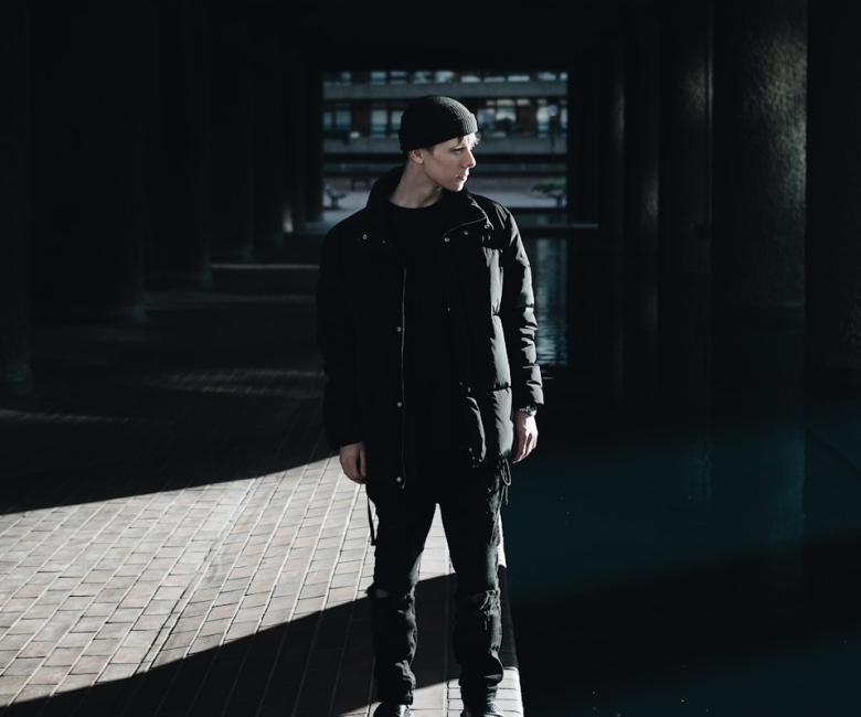 man standing beside gray wall during daytime